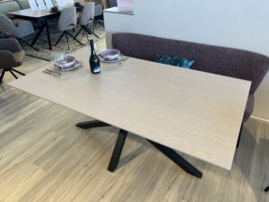 Holztisch mit schwarzen t´Tischbeinen, welche sich in der Mitte des Tisches befinden
