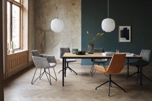 Esszimmer mit großem Holztisch und Stühlen mit grauem Stoffbezug sowie einem Stuhl mit orangenem Leder