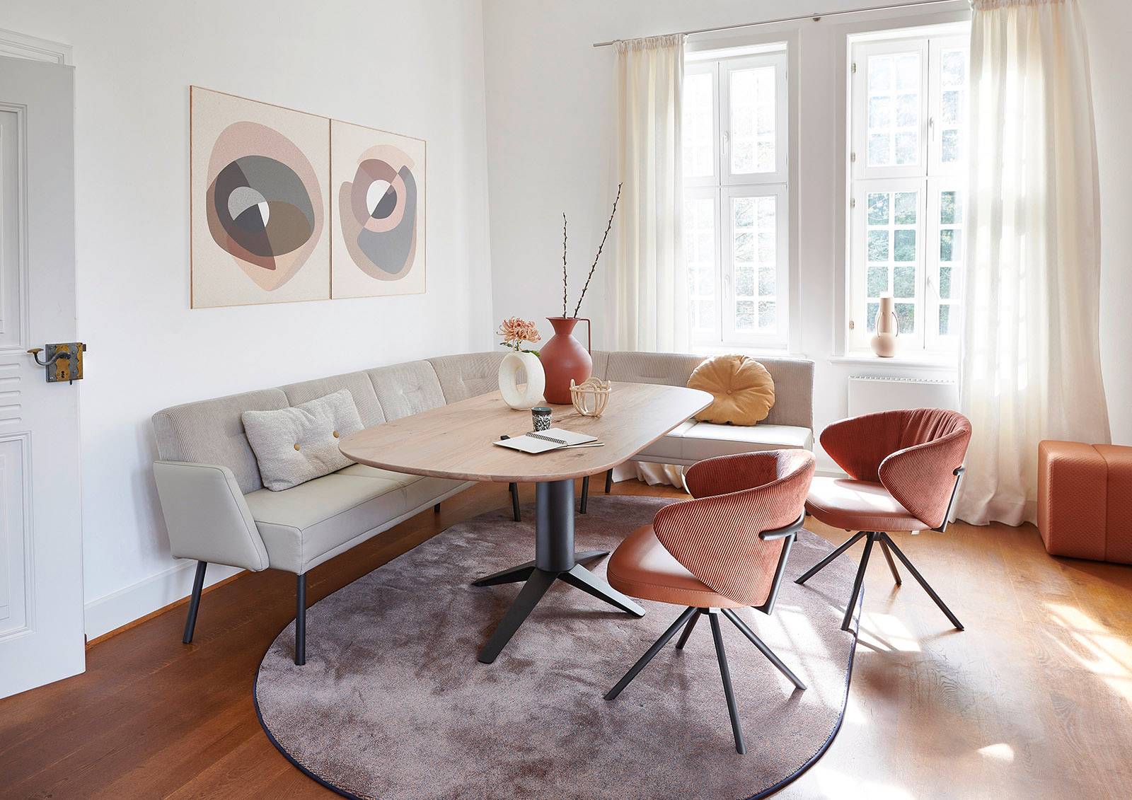 Modernes Esszimmer bei Möbel Polt: Essgruppe mit heller Eckbank, ovalem Holztisch und terracottafarbenen Stühlen.