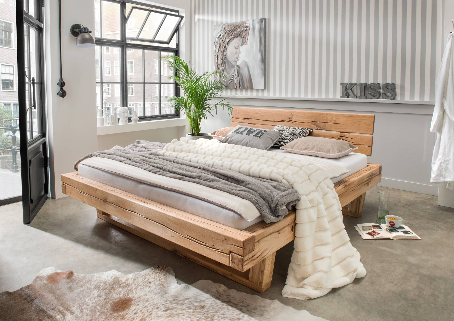 Modernes Massivholzbett von Möbel Polt in hellem Schlafzimmer, Teil der Wohntrends 2026, mit Kuscheldecken und Streifentapete.