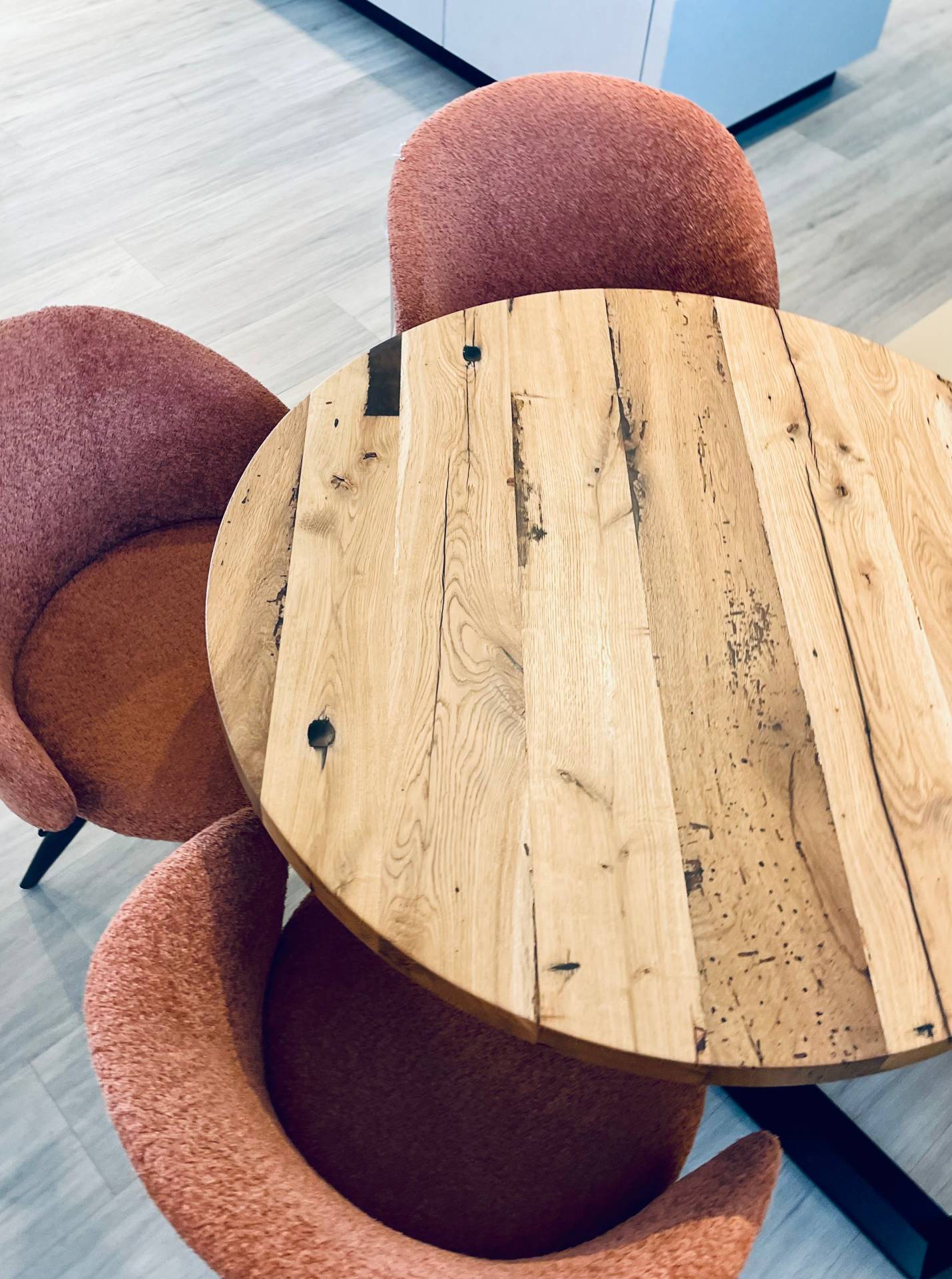 Runder Holztisch mit natürlicher Maserung und drei rötlichen Polstersesseln, Wohntrends 2026 von Möbelpolt.